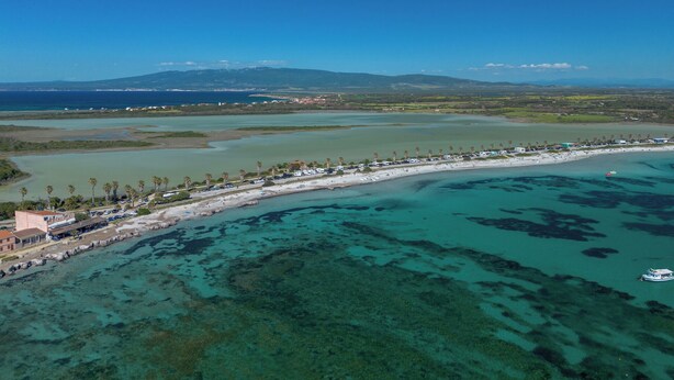 An aerial view of a coastal area with a beach, clear waters, and a distant mountain range. - Just 50 steps from the beach: Vacation Home for 9 Guests & BBQ (Mandriola)