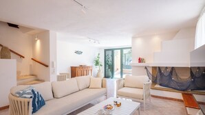 A modern living room with a sofa, coffee table, and chairs, a staircase, and a view through a glass door. - Just 50 steps from the beach: Vacation Home for 9 Guests & BBQ (Mandriola)