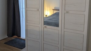 Une chambre avec une grande armoire, un lit, une table de chevet et une fenêtre avec des rideaux.