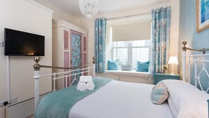 Een hotelkamer met een bed, een televisie, een raam met gordijnen en een kroonluchter.