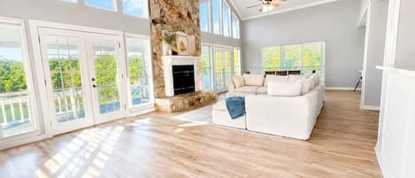 A spacious living room with a stone fireplace, a white sofa, and large windows.