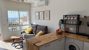 Une cuisine moderne dotée d’un lave-linge encastré, d’un plan de travail en bois et offrant une vue sur la mer grâce à de grandes fenêtres.