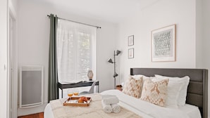 Ein Hotelzimmer mit einem Bett, einem Schreibtisch mit Stuhl, einem Fenster mit Vorhängen und einer Heizung.
