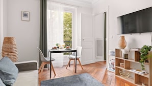 Ein Wohnzimmer mit Esstisch, Stühlen, einer Couch, einem Fernseher und einem Bücherregal.