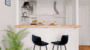 Eine kleine Küche mit einer Holz Arbeitsplatte, zwei schwarzen Stühlen und einem Topf mit Pflanze.