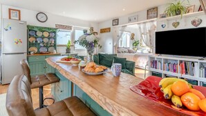Een keuken met een houten aanrecht, barkrukken, een koelkast, een klok en een boekenkast vol boeken.