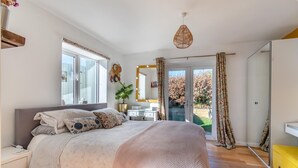 Een slaapkamer met een bed, nachtkastjes, een kaptafel, een spiegel, een kamerplant en een schuifdeur naar een balkon.