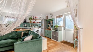 Een gezellige woonkamer met een groene bank, een keuken met een wasmachine, en een eetgedeelte met een tafel.