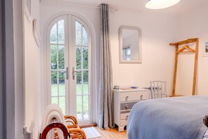Quarto com cama, penteadeira, cadeira, espelho e porta que dá para um jardim.