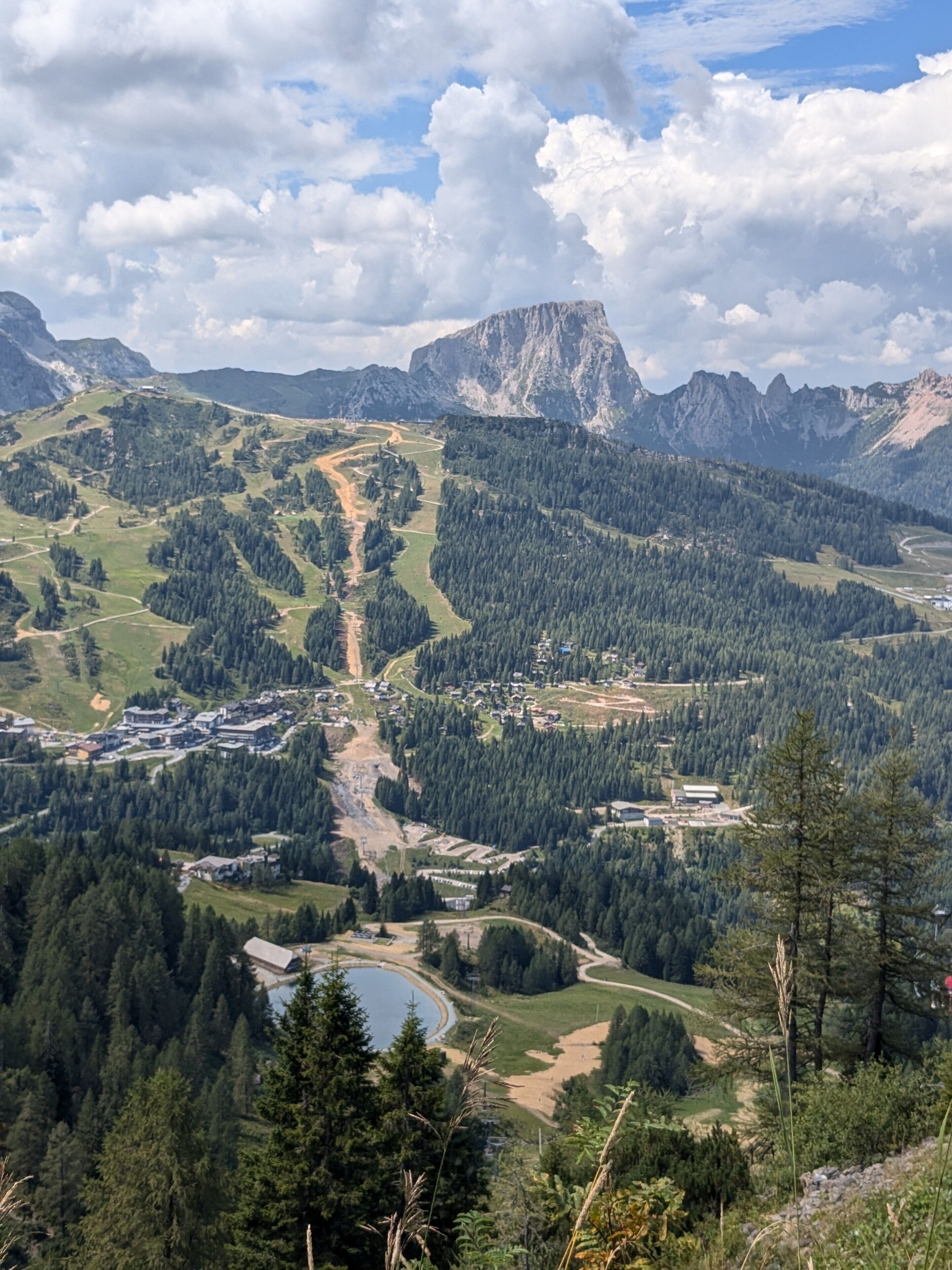 Un paysage montagneux avec une route sinueuse, un lac et une grande montagne en arrière-plan.