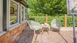 Pieni patio, jossa on kaksi tuolia, pöytä ja pieni puutarha-alue.