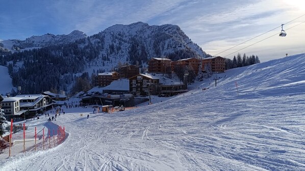 Une station de ski comprenant plusieurs bâtiments, des remontées mécaniques et un paysage montagneux enneigé en toile de fond.