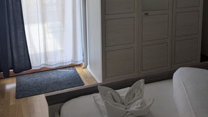 Un dormitorio con cama, armario, ventana con cortinas translúcidas y alfombra oscura.