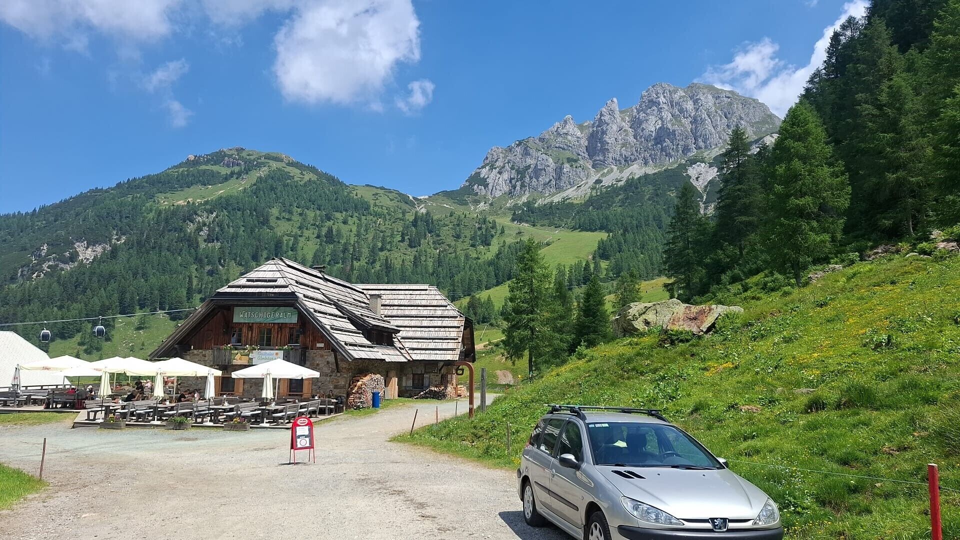 A mountain lodge with outdoor seating, a car parked in front, and a view of the surrounding mountains.