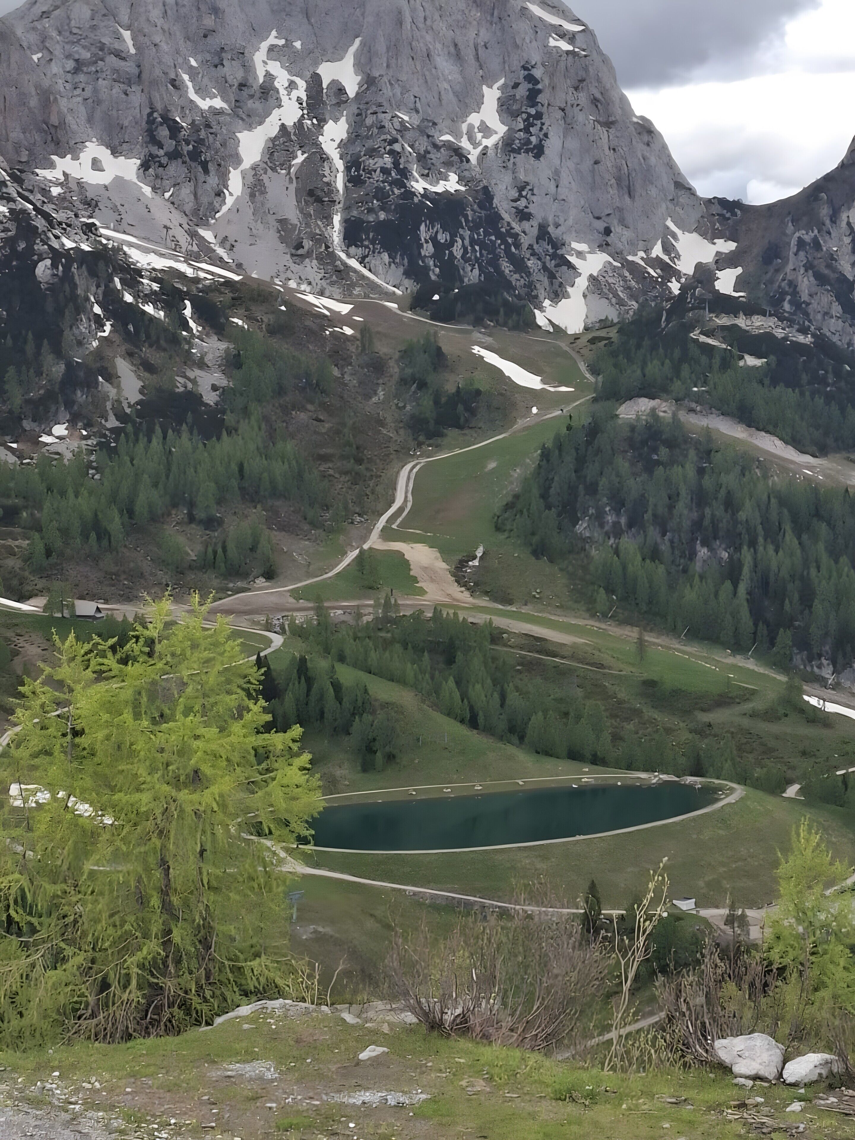 A mountainous landscape with a winding road, a lake, and dense forest.