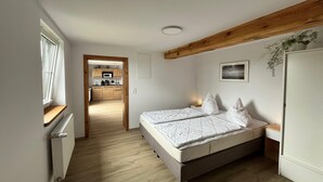 A bedroom with a bed, a wooden ceiling beam, a small bedside table, and a window. - Neues Appartement im Lepels Hof (Lütow)