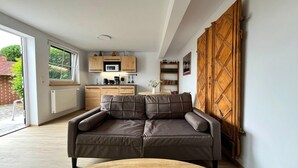 A modern living room with a sofa, a wooden coffee table, a kitchen area with cabinets and a microwave, and a large wooden door. - Neues Appartement im Lepels Hof (Lütow)