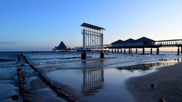 A pier extending into the water with a structure on it, a sandy beach, and a clear sky. - Neues Appartement im Lepels Hof (Lütow)