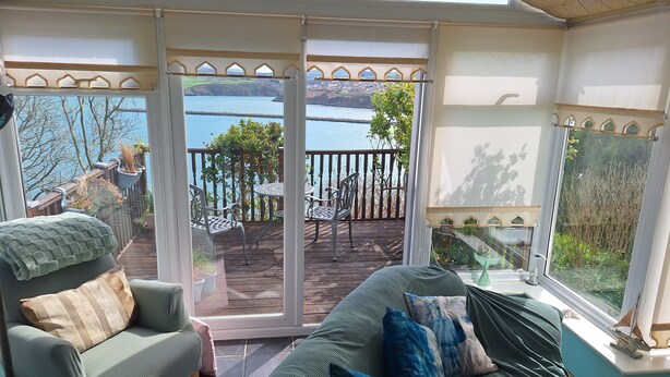 A room with a sofa, a chair, a small table, and a view of a lake through a glass door. - Private self catering apartment close to the stunning Pembrokeshire coast path. (Goodwick)