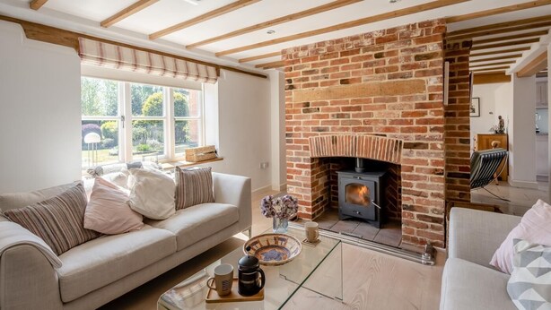 A living room with a brick fireplace, a sofa, a coffee table, and a window with a view of greenery. - 3 Bed in Orford (oc-t32016) (Orford)