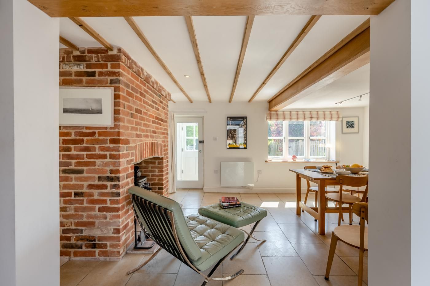 Une pièce avec une cheminée en briques, un canapé en cuir vert, une table à manger avec des chaises et une fenêtre donnant sur l’extérieur.