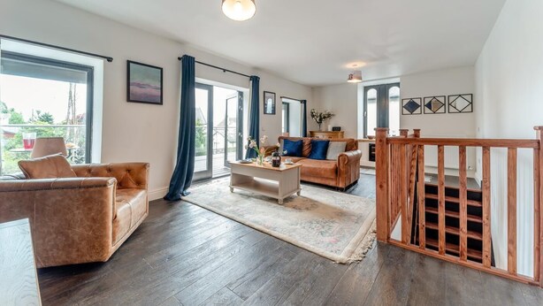 Un amplio salón con suelo de madera, un conjunto de sofás, una mesa de centro y una escalera con barandilla de madera.