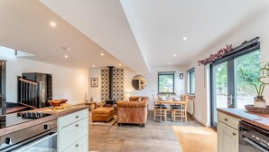 Una cocina moderna con estufa integrada, un comedor con mesa y sillas de madera, un sofá y un ventanal con vistas a zonas verdes.