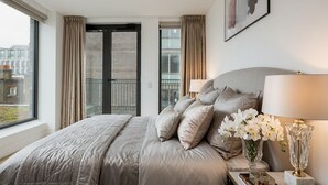 Een slaapkamer met een bed, gordijnen, een raam, een lamp en een vaas met bloemen.