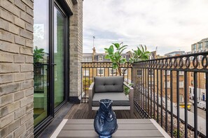 A balcony with a sofa, a decorative vase, and a view of the cityscape. - The Fitzrovia Grand Residence (London)