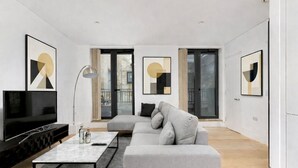 Een moderne woonkamer met een flatscreen televisie, een grijze bank en abstracte muurkunst.