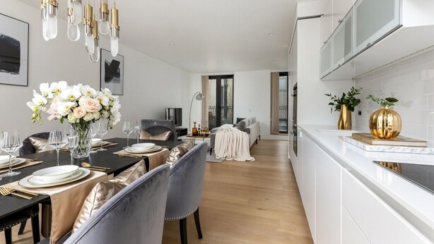 Een moderne keuken met witte kasten, een eethoek met een lange tafel voor zes personen, en een woonkamer met een bank en een salontafel.