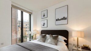 Een moderne slaapkamer met een groot bed, een glazen bijzettafeltje en lijstwerken aan de muur.