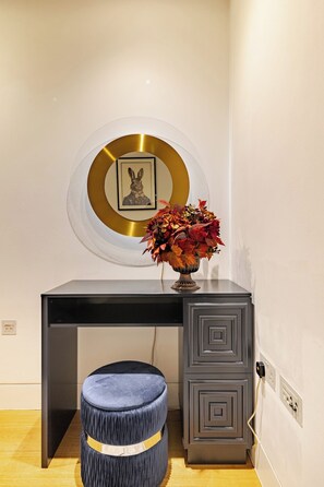 A desk with a vase of flowers, a framed picture, and a circular decorative element on the wall. - The Fitzrovia Grand Residence (London)