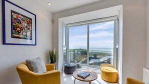 A modern living room with yellow chairs, a glass door leading to a balcony, and a framed abstract artwork on the wall. - 4 Bed in Saltdean (oc-a32366) (Saltdean)