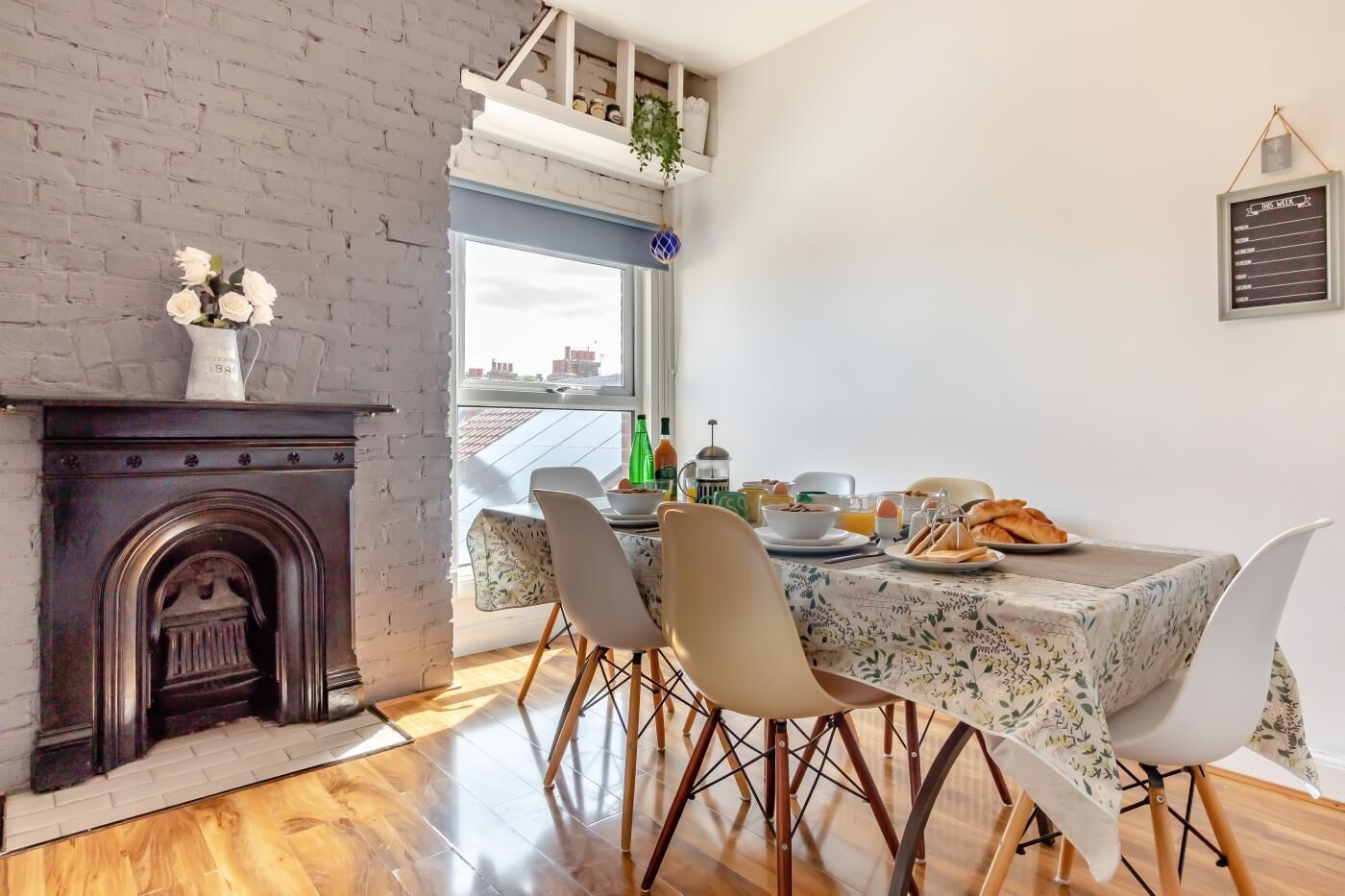A dining area with a table set for breakfast, a fireplace, and a view through a window.
