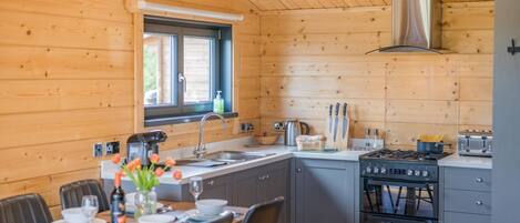 A wooden cabin interior with a kitchen, dining area, and a window with a view.