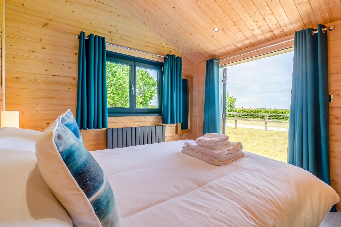 Ein Zimmer mit Holzwänden, einem Bett, einem Fenster mit Vorhängen und Blick auf einen Weinberg.