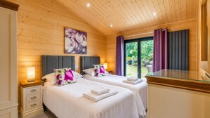 Habitación de hotel con dos camas, paredes de madera, un ventanal con cortinas y un cuadro colgado.