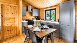 Una cocina compacta con paredes de madera, una mesa de comedor lista para cuatro personas y una ventana con vistas a la vegetación.
