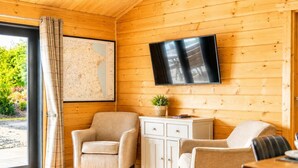 Interior acogedor de una cabaña con pared de madera, un televisor de pantalla plana, un mapa, un sofá, una silla y una pequeña mesa.