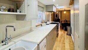A modern kitchen with a large island, built-in appliances, and a dining area in the background. - 17th Century Cottage | Suffolk Market Town (Hadleigh)