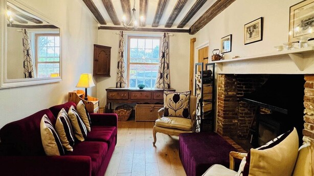 A living room with a fireplace, wooden beams, a sofa, a chair, and a desk. - 17th Century Cottage | Suffolk Market Town (Hadleigh)