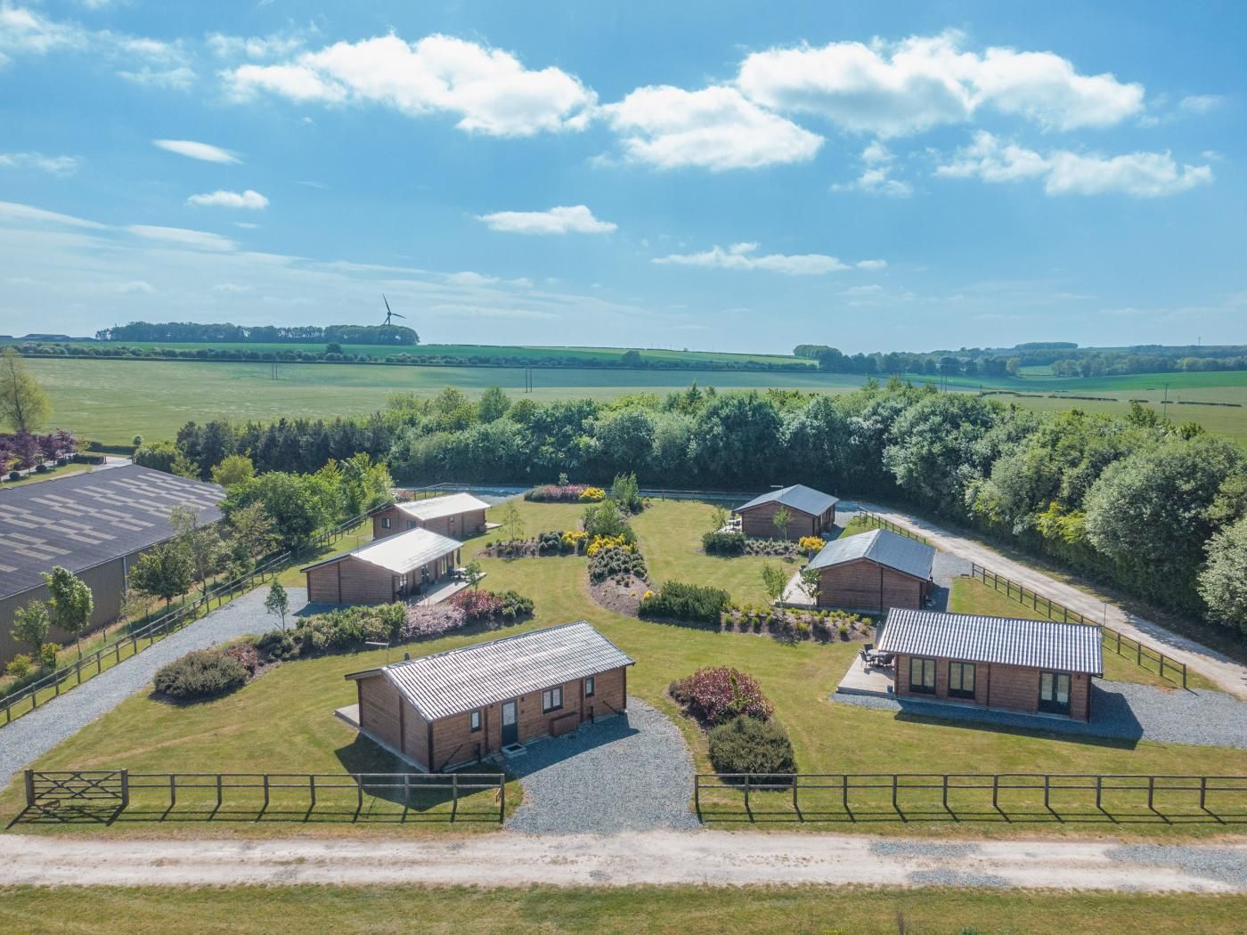 A rural property with multiple buildings, a large open field, and a wind turbine in the distance.