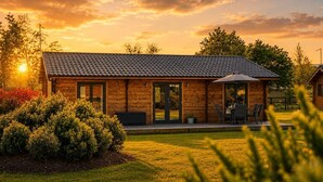 En træhytte med et tagdækket tag, en terrasse med udendørs møbler og en velplejet græsplæne.