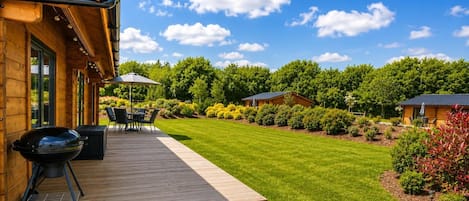 Una terraza de madera con mobiliario exterior, una parrilla y un césped cuidado.