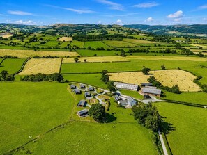 Ländliche Landschaft mit Feldern, einer kleinen Gebäudegruppe und fernen Hügeln.