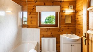 A wooden cabin bathroom with a bathtub, a sink, a window, and a radiator. - 2 Bed in Llandinam (oc-t31972) (Llandinam)