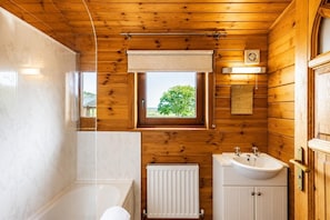 Ein Badezimmer einer Holzhütte mit einer Badewanne, einem Waschbecken, einem Fenster und einer Heizung.
