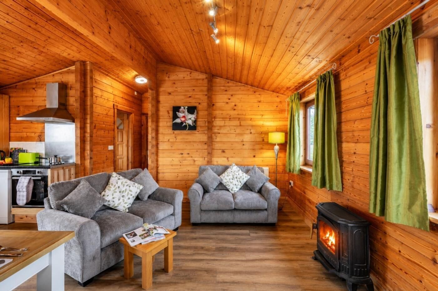 A cozy cabin interior with two sofas, a table, a fireplace, and a kitchen area.