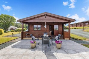 Eine Holzhütte mit einer Terrasse, ausgestattet mit Tisch und Stühlen, umgeben von einem Kiesweg.